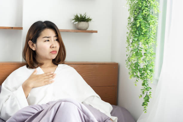 unwell Asian woman suffering from nausea, sore throat in morning unwell Asian woman suffering from nausea, sore throat in morning sitting in bed nausea stock pictures, royalty-free photos & images