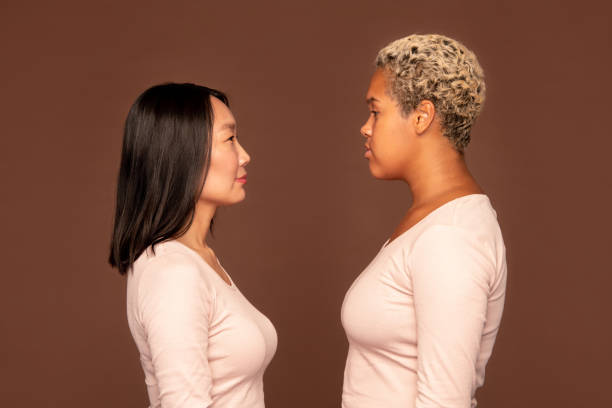 istock Side view of two young intercultural women in white pullovers in front of camera 1288255400