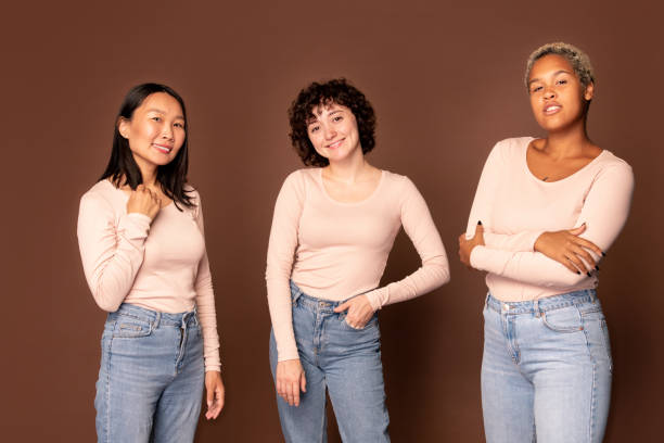 istock Young joyful women in white pullovers and blue jeans standing in front of camera 1288255409