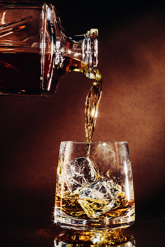 Pouring a glass of whisky with ice, from a decanter in a dark background.