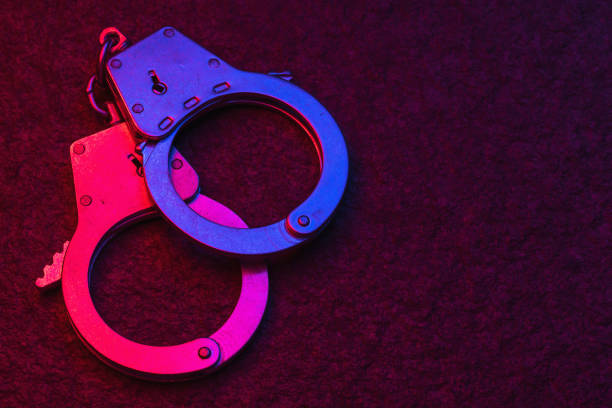 Handcuffs on dark background illuminated by flashing lights of police car with copy space stock photo