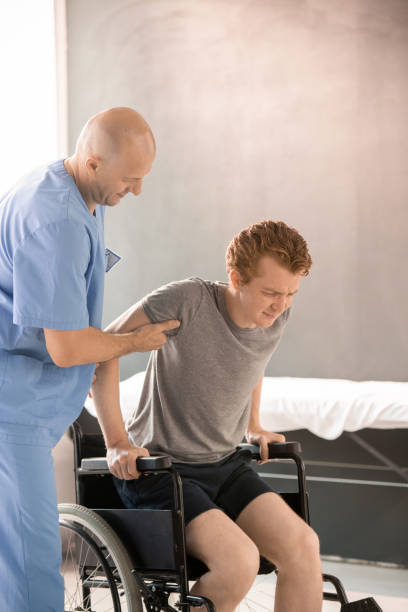 istock Bald physiotherapist helping sick young man to sit in wheelchair after training 1288258607