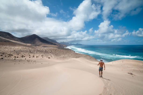 giovane cammina tra le dune di jandia verso le montagne di cofete. fuerteventura. - light sea low tide fuerteventura foto e immagini stock