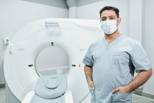 Successful young mixed-race male doctor in protective mask and uniform Successful young mixed-race male doctor in protective mask and uniform standing in front of camera against ultra sound equipment oncology photos stock pictures, royalty-free photos & images