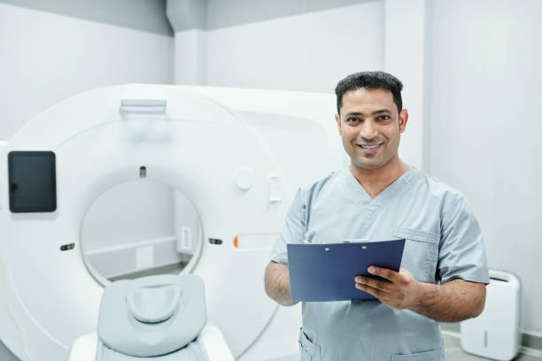 felice maturo medico maschio di razza mista in uniforme blu facendo appunti nel documento - radiologist foto e immagini stock