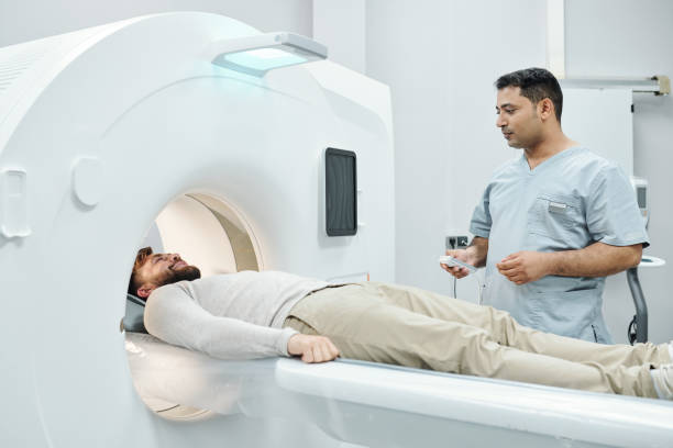 joven médico masculino de raza mixta en el botón de tocar uniforme médico en el panel de control - tomografía fotografías e imágenes de stock