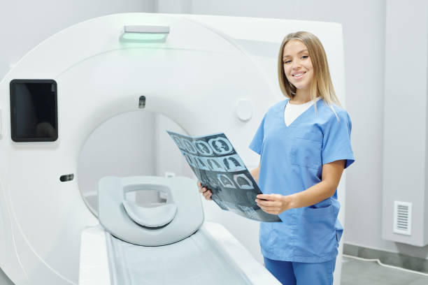 x線画像を分析する青い均一の幸せな若いブロンドの女性放射線科医 - radiologist cat scan x ray cat scan machine ストックフォトと画像