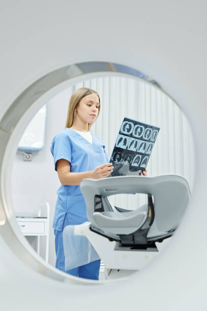 joven radiólogo en uniforme mirando la imagen de rayos x de la cabeza del paciente y el cerebro - mri scan radiologist cat scan cat scan machine fotografías e imágenes de stock