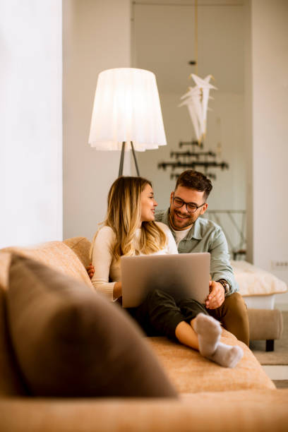istock Young couple using laptop together while sitting on sofa at home 1288263692