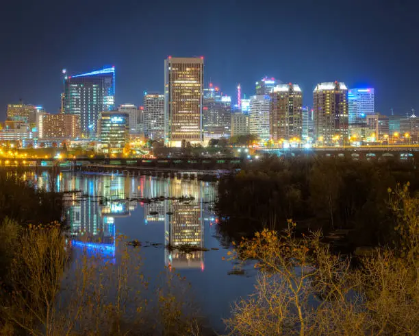 The skyline of Richmond Virginia is seen at night.  The lights of the buildings are reflected on the James River.