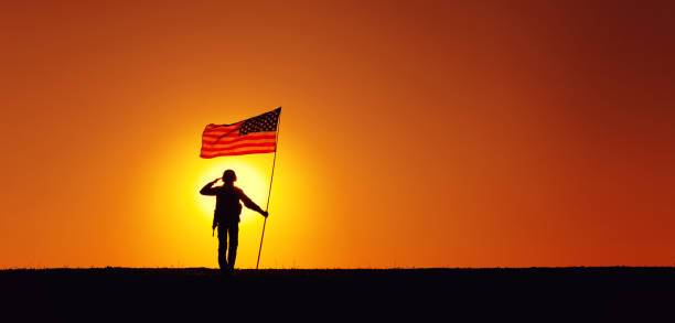 USA Soldier with flag saluting on sunset horizon Silhouette of USA armed forces soldier, army infantryman or Marine Corps fighter saluting while standing with waving national flag on sunset background. Military victory and glory, fallen remembrance militant groups photos stock pictures, royalty-free photos & images