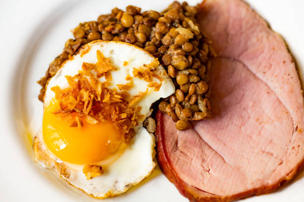 Sliced smoked meat, fried egg with onion and lentil on white plate stock photo