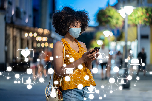 Young Afro-American woman wearing protective face mask using smart phone. Social media concept.