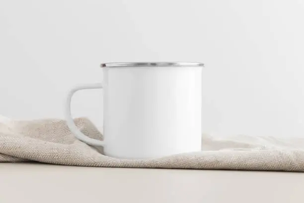 Enamel mug mockup with a table cloth on a beige table.