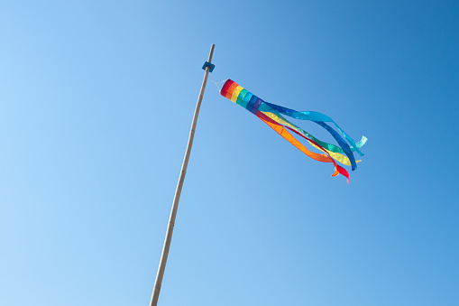 Rainbow colored wind sock fluttering in the wind on a clear blue sky day