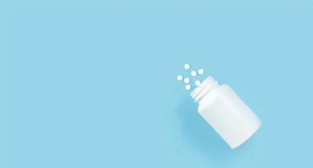 Medicine bottle and white pills spilled on a light blue background. Medicines and prescription pills flat lay background. High quality photo