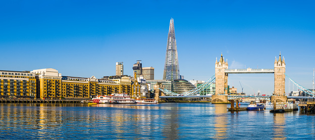 Panoramic view across the River Thames to the historic span of Tower Bridge illuminated by warm early morning sunlight overlooked by the futuristic glass spire of The Shard in the heart of London, Britain's vibrant capital city.