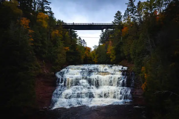 Photo of Close up aerial view of Agate Falls waterfall with an abandoned railroad bridge crossing above surrounded by evergreen and deciduous trees with fall colored foliage on a cloudy day in Upper Michigan.