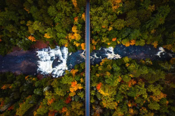 Photo of Beautiful look down travel aerial photograph of the abandoned railroad bridge crossing the Ontonagon River and scenic Agate Falls waterfall below surrounded by forest of evergreen and deciduous trees.