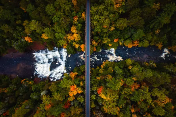 Photo of Beautiful autumn look down travel aerial of a man laying down on the abandoned railroad bridge crossing the Ontonagon River and scenic Agate Falls waterfall below surrounded by forest of trees.