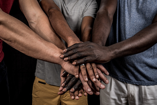 Multiracial group of adult friends or colleagues putting their hands together. People stacking hands to show unity and teamwork. Cooperation and success concept.