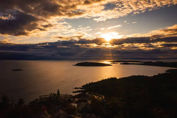 Photo of Beautiful sunrise aerial photograph above Sugarloaf Mountain looking towards Presque Isle peninsula and islands in Lake Superior with the sun shining between clouds and reflecting off of the water.