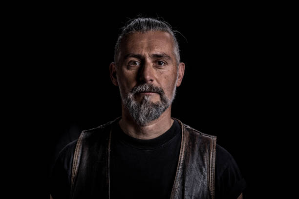 Portrait of serious Caucasian guy looking to camera. Bearded mature adult man against black background.