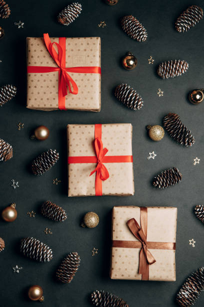 istock Christmas composition with a gift in a box. Golden toys, modern holiday decorations, gift boxes, fir branches on a dark black background. Elegant Christmas greeting card template. 1288286864