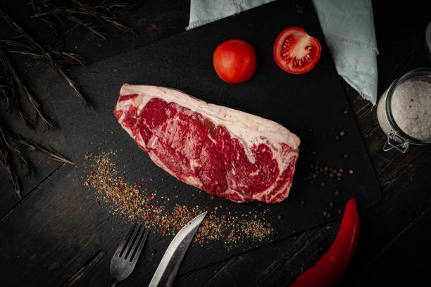 Raw ribeye beef steak on a black plate.