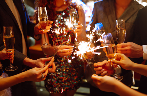 Sparkling sparklers in the hand. Group of happy people holding sparklers at the party. Young friends clinking glasses of champagne  in a nightclub. Celebration, people and holidays concept.