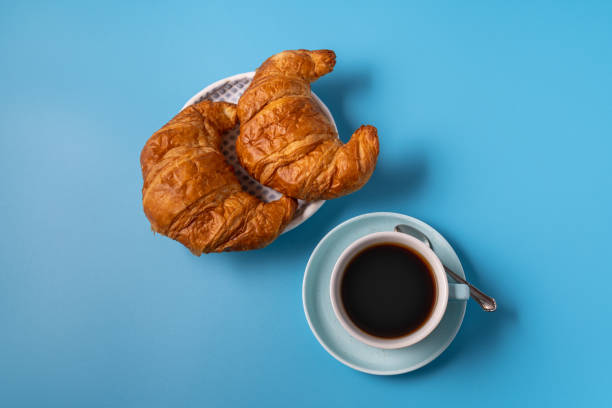 istock Cup of black coffee and croissant on blue background, copy space for text 1288293123