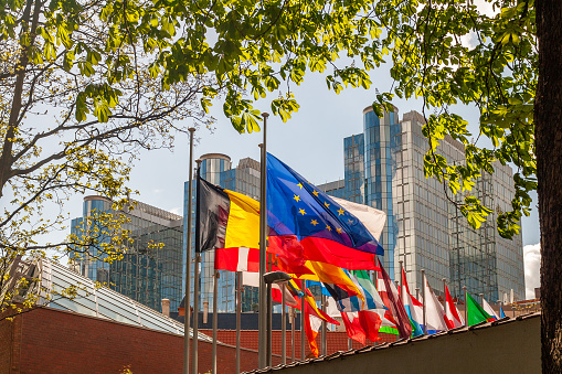 A row of back-lit flags in front of the glass facade of the Paul Henri Spaak building of the European Parliament in Brussels.\