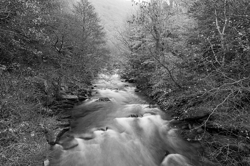 Kent Falls in Connecticut. Long view of upper falls after rain, early spring. Widely considered the most spectacular waterfall in the state and one of the best in New England. In rural Litchfield County, Kent Falls is a popular state park. You park near the bottom of the half-mile trail and follow it to the top, with viewing platforms along the way. The falls are 250 feet high. Black-and-white photo.