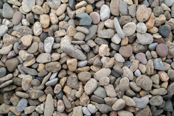 texture of a natural assortment of pebbles and river stones in warm earth tones, ideal for landscaping, garden borders, pathways, or decorative rock surfaces. Natural Pebbles And River Stones For Landscaping And Garden Decor