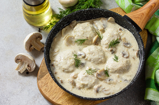 Homemade meatballs in sour cream sauce with mushrooms in a pan on stone or slate table.