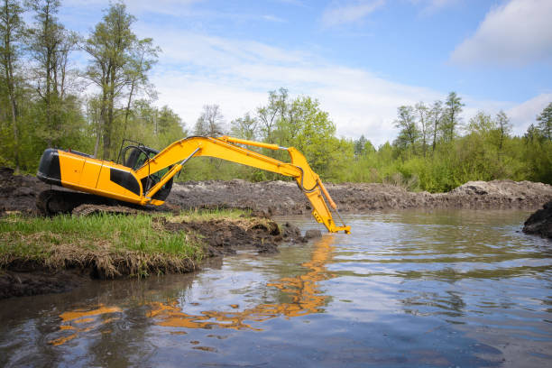 istock Big excavator puts its shovel under the water to dig make river canal more deep and clean it of different garbage 1288302035