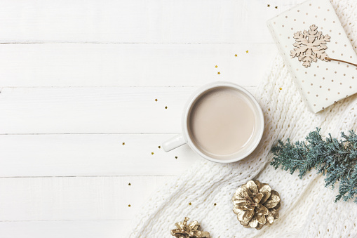 Cozy morning moments at home with cup of coffee, warm blanket, evergreen tree and ornaments on white wooden background. Winter, holidays concept. Flat lay, top view, copy space.