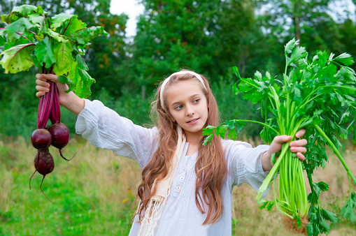 1 European girl 11 years old holding fresh beets and celery on a green background