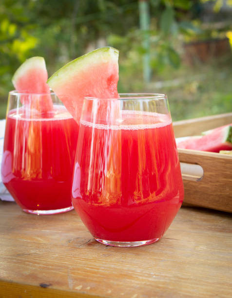 Two glasses with fresh watermelon smoothie and watermelon slices on wooden table in summer garden Two glasses with fresh watermelon smoothie and watermelon slices on wooden table in summer garden watermelon juice stock pictures, royalty-free photos & images