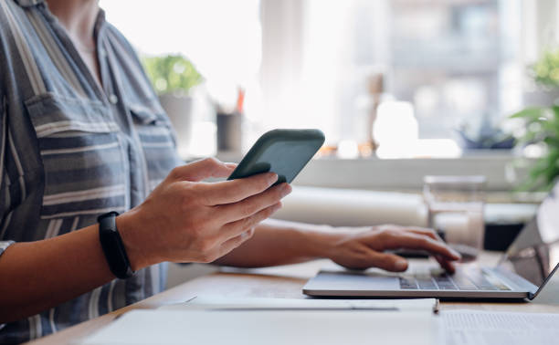 istock Close up Shot of an Anonymous Young Businesswoman's Hands Using a Mobile Phone while Working from Home on a Laptop 1288318049