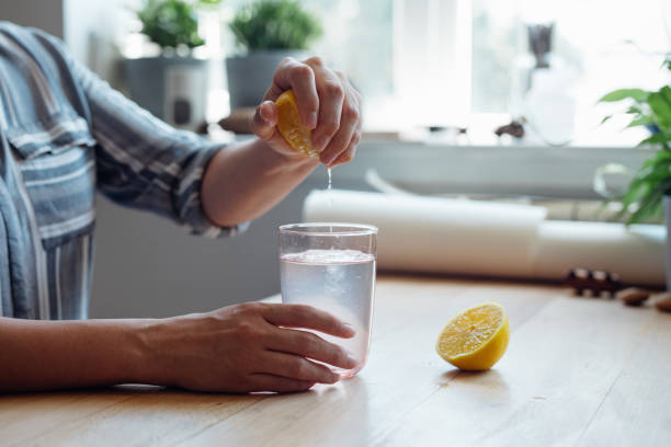 fermez-vous vers le haut le projectile d’une jeune femme anonyme serrant un citron dans une tasse d’eau faisant la limonade - waterlemon photos et images de collection