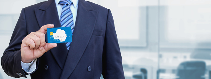 Cropped image of businessman holding plastic credit card with printed flag of Antarctica. Background blurred.