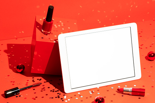 Digital tablet mockup, template and makeup cosmetics on red background with Christmas balls and confetti