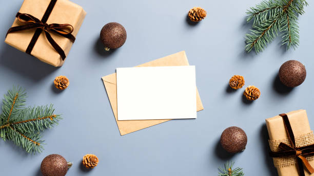 istock Blank paper card mockup, envelope, craft paper gift boxes, pine tree branches and Christmas decorations on pastel blue background. Christmas or New Year greeting card concept 1288326054