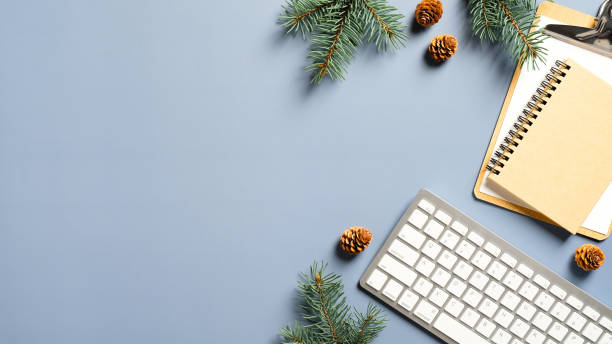 istock Cozy home desk table with keyboard, notebook, Christmas tree branches, cones on blue background. Top view, flat lay, copy space. Winter composition. Nordic hygge style concept 1288326060