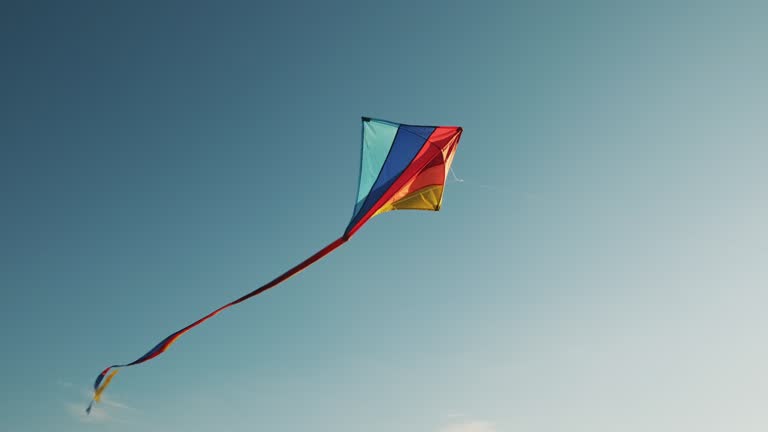 Flying kite against background blue sky at sunset on sunny day in summer. Lens flare. City kite festival. Tail of kite sways in wind. Childhood. Freedom. Toy. Relax