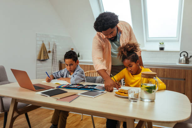istock Afro students doing homework at home with school books helped by their father. Dad control, help and teaching their children 1288333664