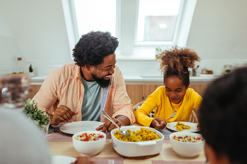 Afro father and daughter sitting at the kitchen table and having lunch