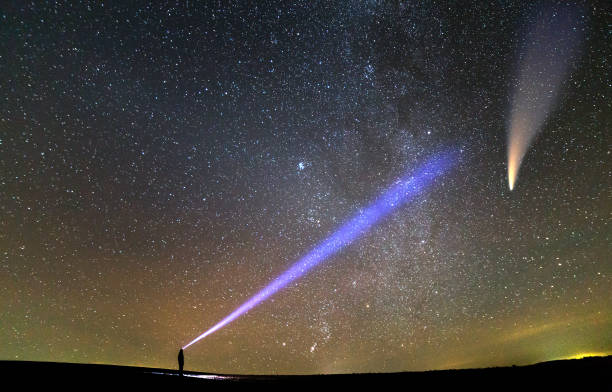 istock Small silhouette of a scientist with flashlight on his head pointing bright beam of light on starry sky with C/2020 F3 (NEOWISE) comet with light tail. Space exploration concept. 1288333876