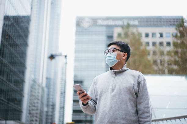 istock Asian business man wearing a protective mask looking up and planning his schedule while holding his smartphone at the financial area of the city. 1288334523